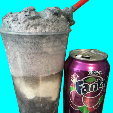 Frozen drink in a clear cup with ice, next to a can of grape Fanta on a metal surface.